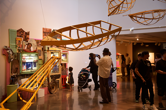 People explore our art gallery, including wooden boat sculptures
